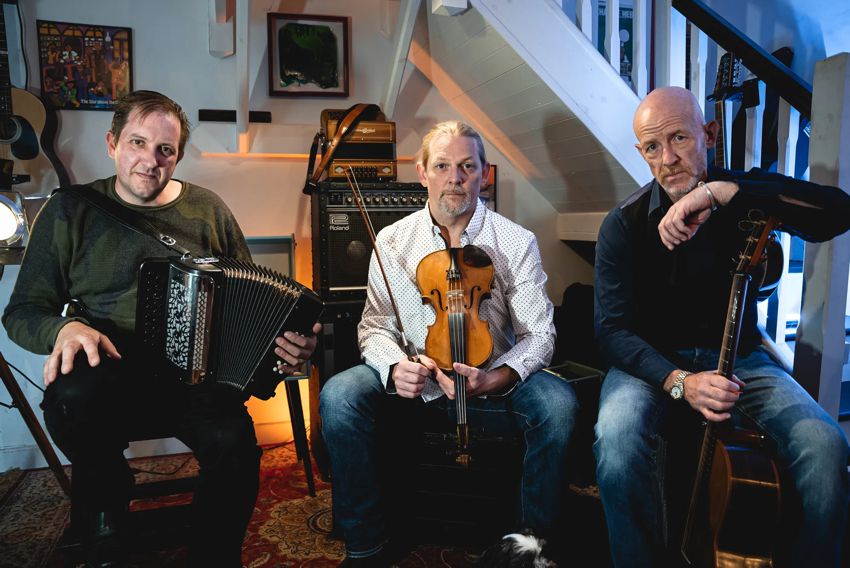 The 3 members of Miscellany of Folk with instruments in front of a staircase.